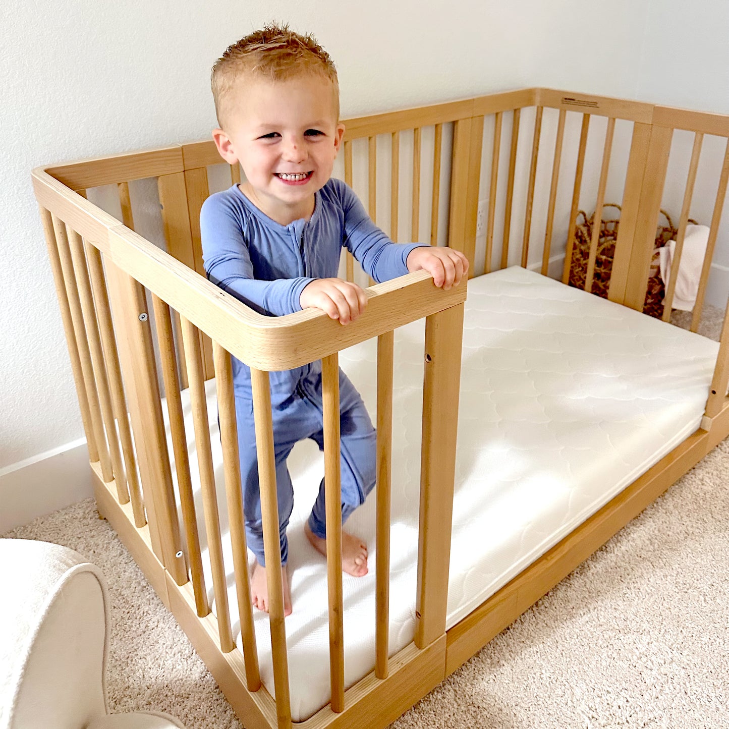 Child smiling and standing up in Newton Nest Convertible Crib in natural color