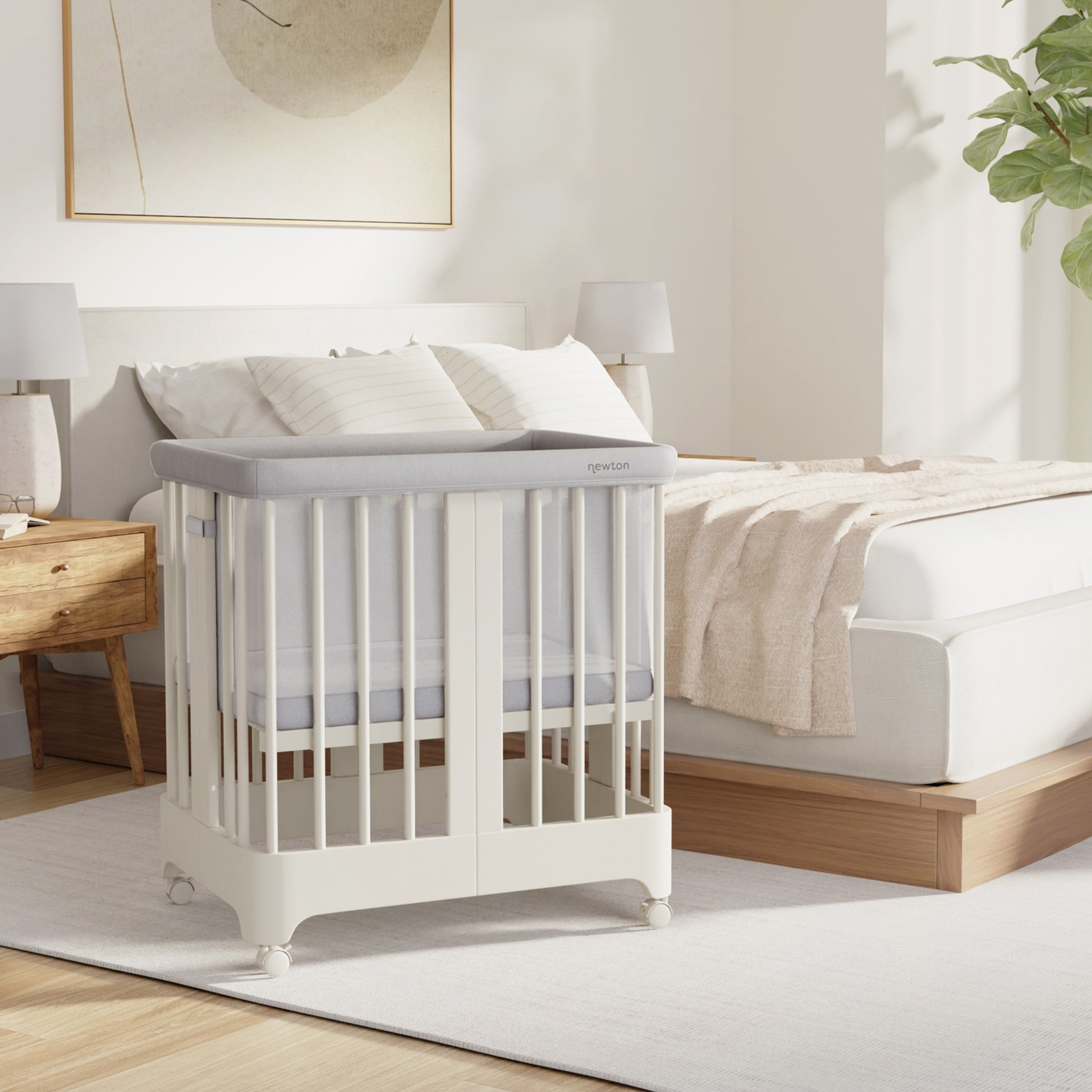 Warm white color Newton Nest Convertible Crib in bassinet setting next to bed in bedroom
