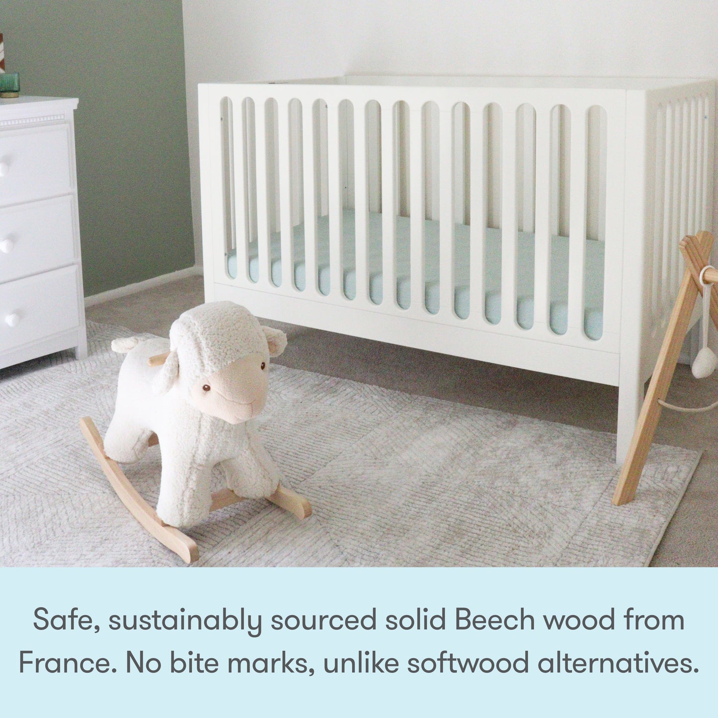 The Newton Galileo Convertible Crib by Newton Baby, made from sustainably sourced solid beech wood from France, stands in a softly lit nursery with a plush rocking sheep on a gray rug, emphasizing its safety and quality craftsmanship.