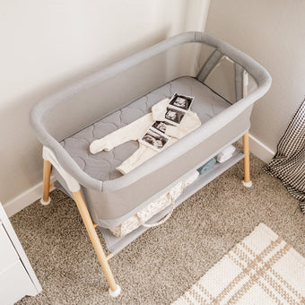 cream onesie with sonogram image on gray bassinet mattress in essential bassinet in a neutral toned room