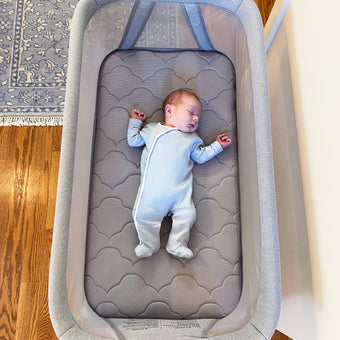 Sleeping baby in gray onesie on gray cloud pattern bassinet mattress for essential bassinet