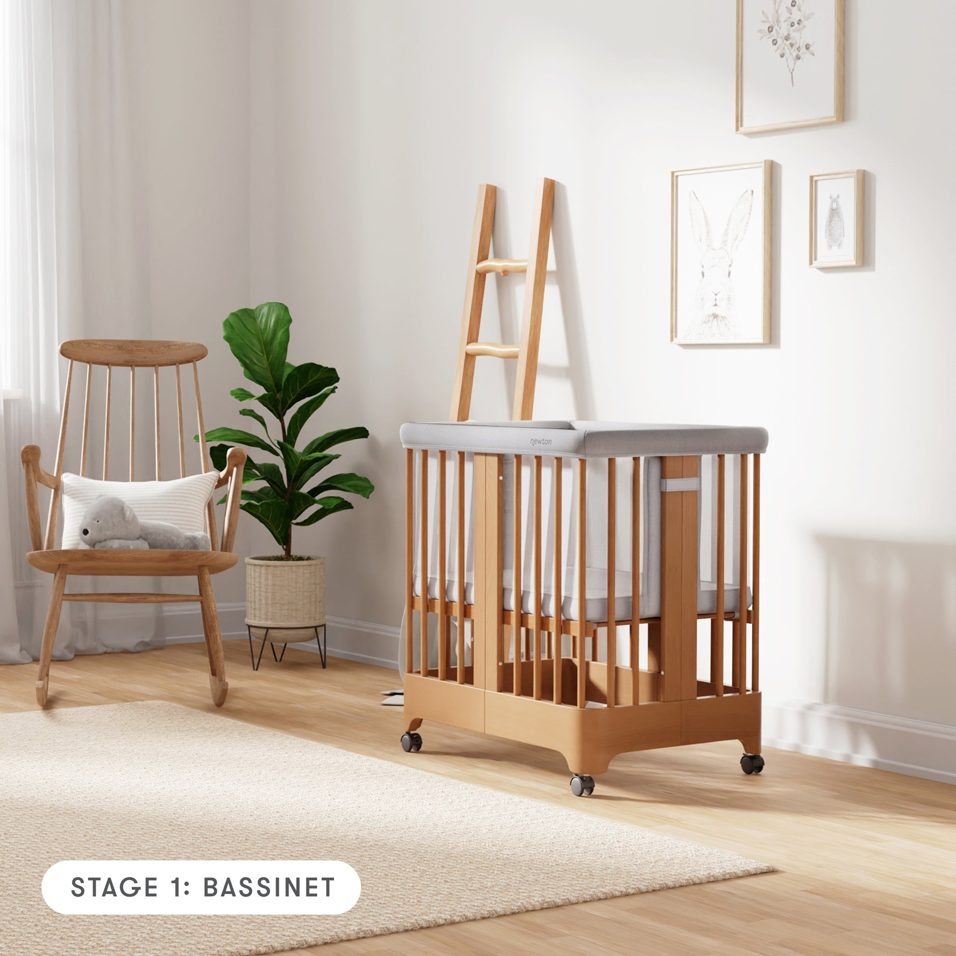 Natural color Newton Nest Convertible Crib in bassinet setting with mesh liner, in nursery next to rocking chair, with text "Stage 1: Bassinet"