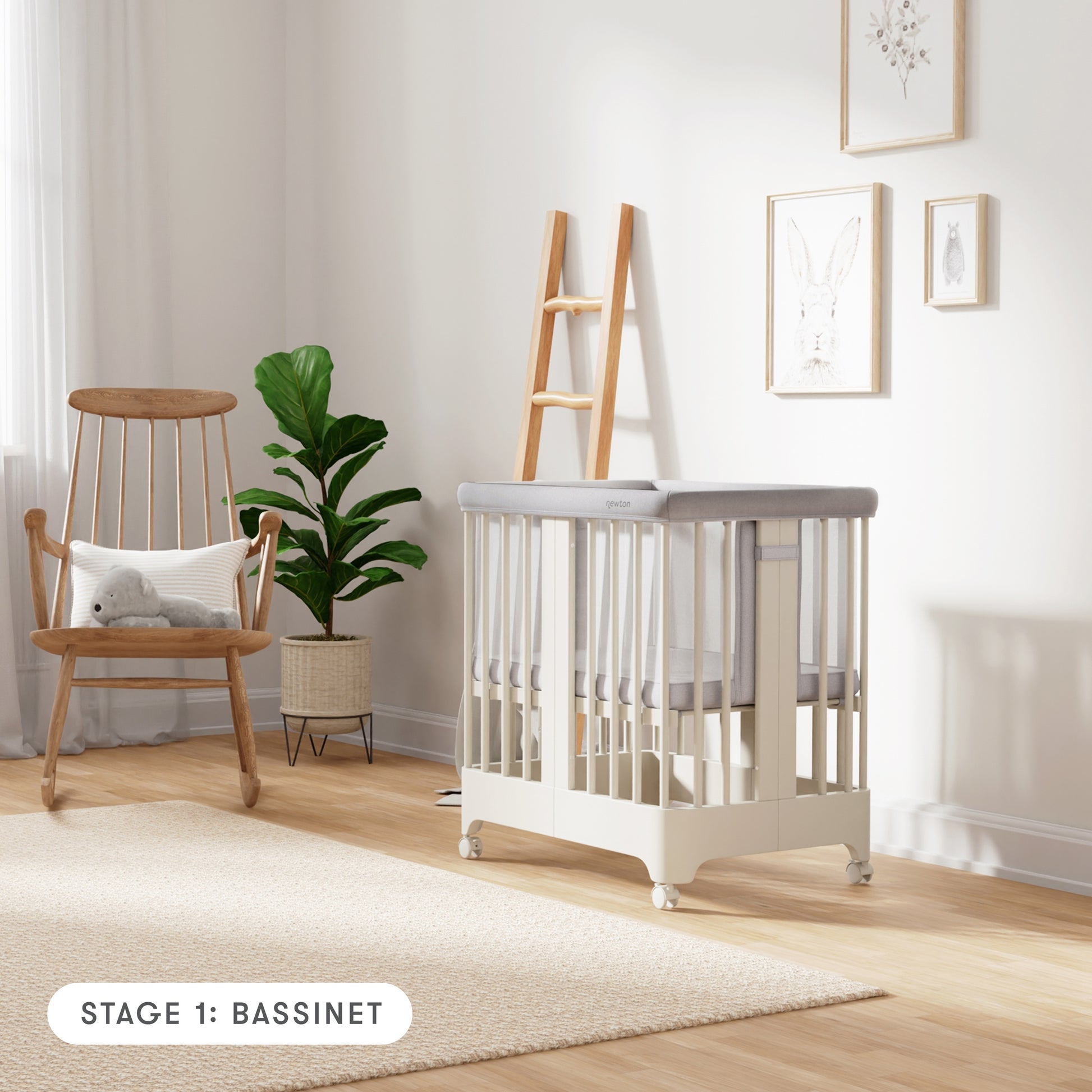 Warm white color Newton Nest Convertible Crib in bassinet setting with mesh liner, in nursery next to rocking chair, with text "Stage 1: Bassinet"