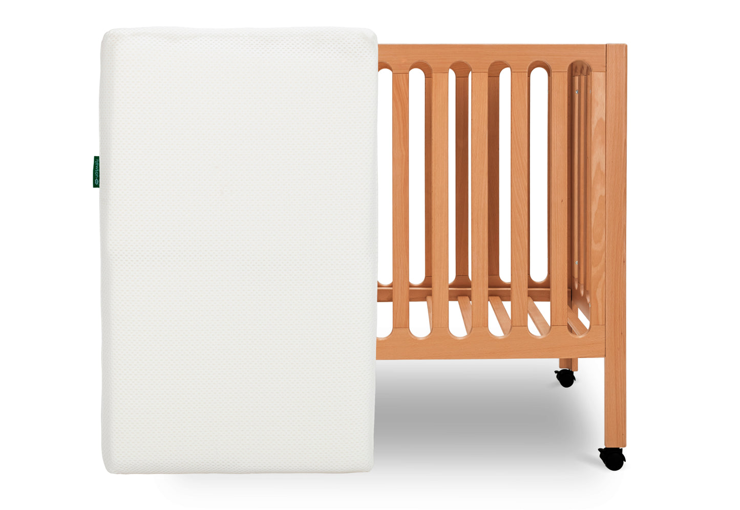 ALT text: "Newton Baby crib mattress placed vertically beside a light wooden crib with wheels on a white background." skip