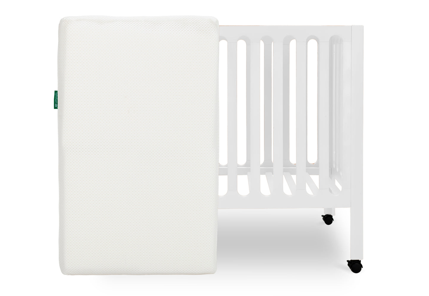 White crib mattress by a crib with slatted sides on a white background. skip
