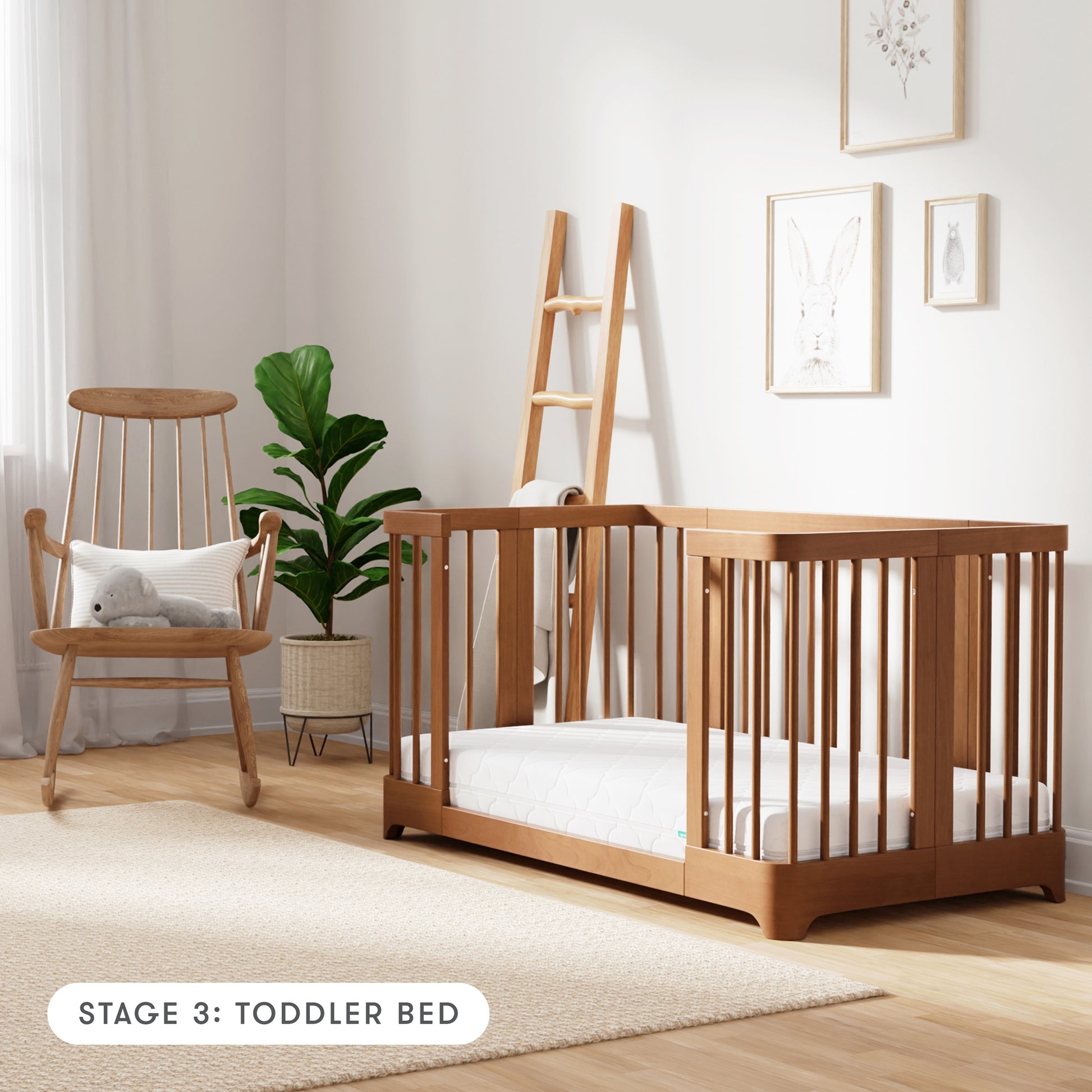 Chestnut color Newton Nest Convertible Crib in toddler bed setting, in nursery next to rocking chair, with text "Stage 3: Toddler Bed"
