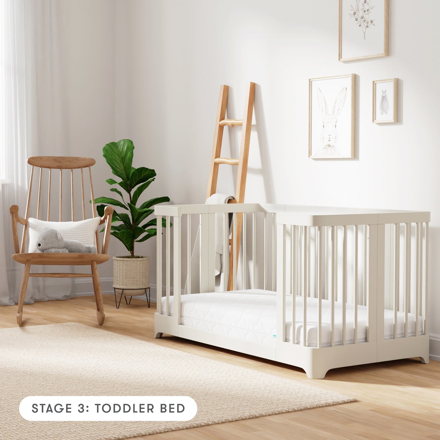 warm white color Newton Nest Convertible Crib in toddler bed setting, in nursery next to rocking chair, with text "Stage 3: Toddler Bed"