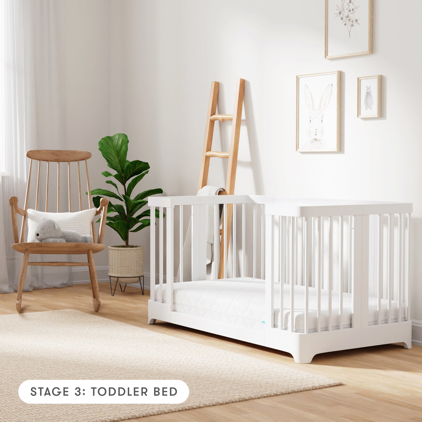 White color Newton Nest Convertible Crib in toddler bed setting, in nursery next to rocking chair, with text "Stage 3: Toddler Bed"