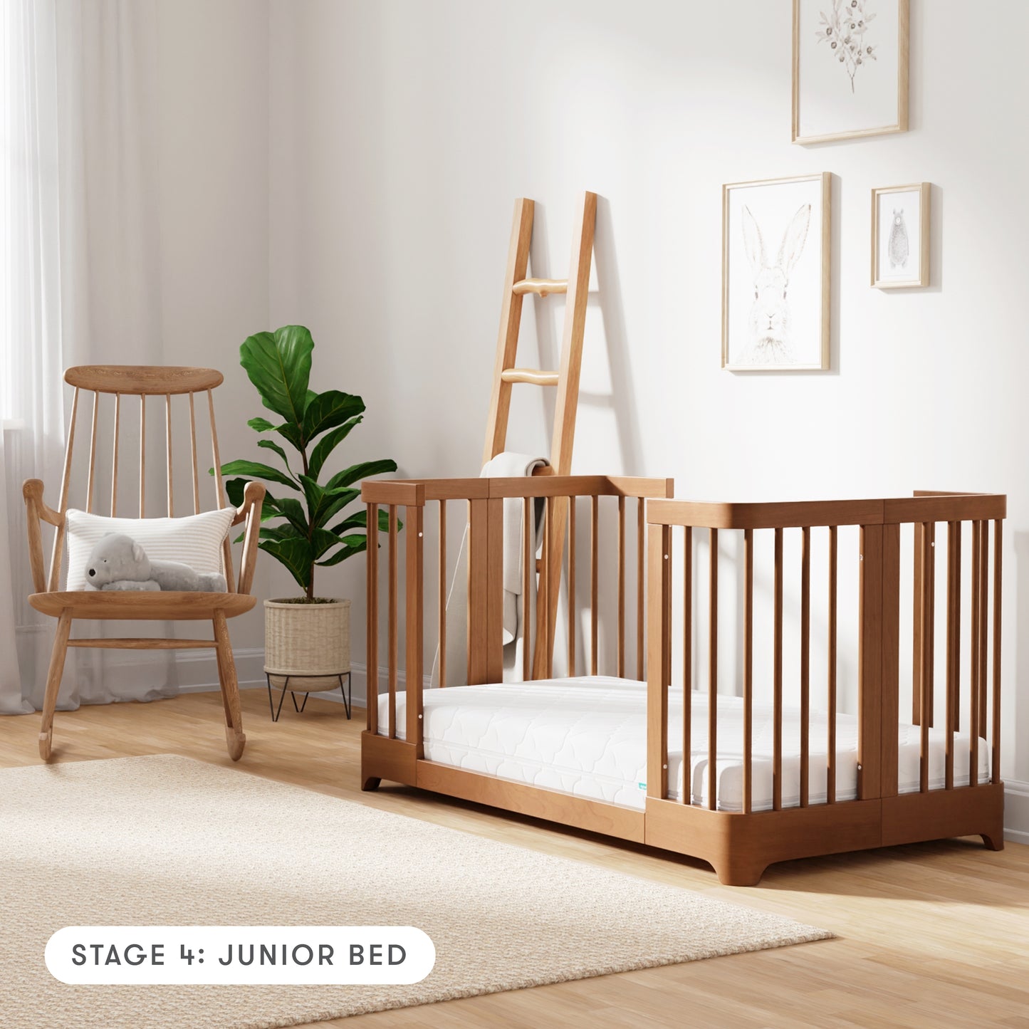 Chestnut color Newton Nest Convertible Crib in Junior Bed setting, in nursery next to rocking chair, with text "Stage 4: Junior Bed"
