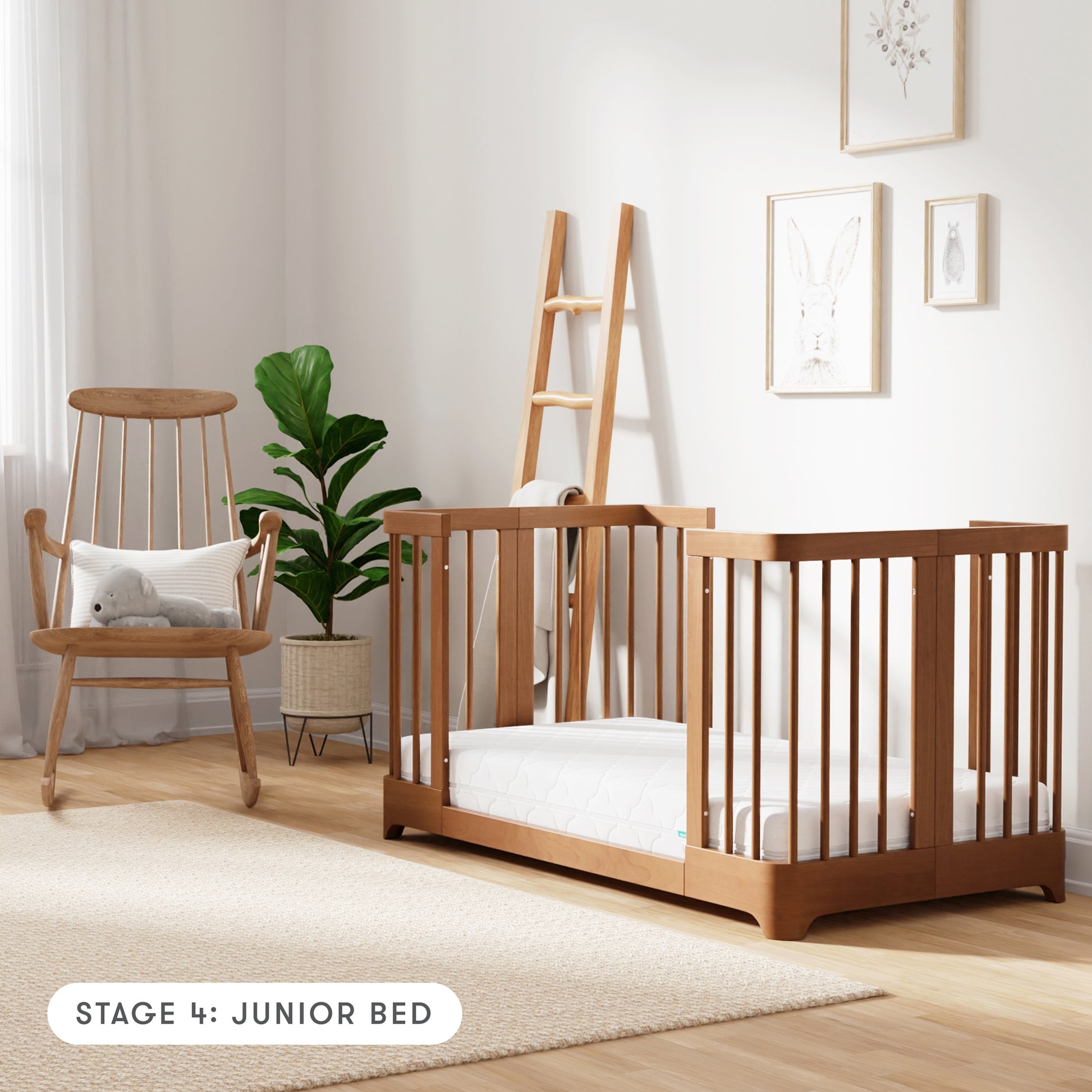 Chestnut color Newton Nest Convertible Crib in Junior Bed setting, in nursery next to rocking chair, with text "Stage 4: Junior Bed"