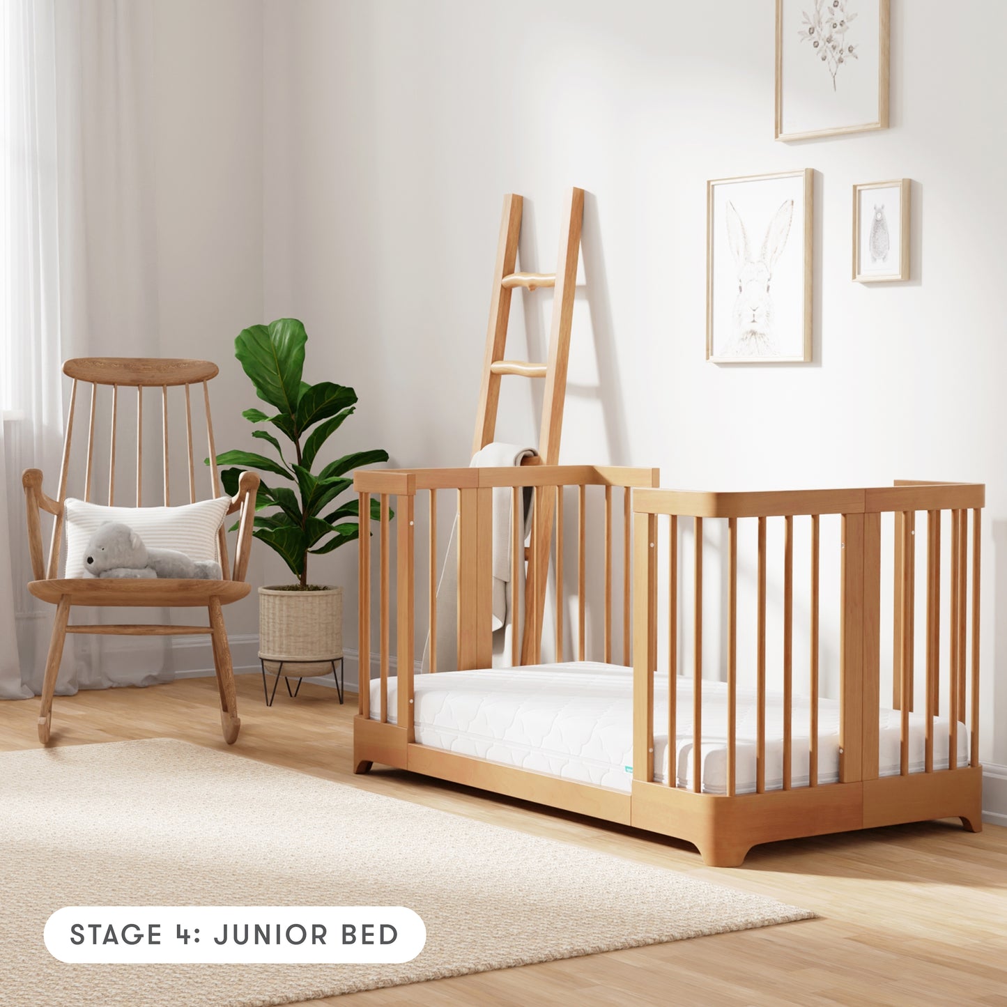 Natural color Newton Nest Convertible Crib in Junior Bed setting, in nursery next to rocking chair, with text "Stage 4: Junior Bed"