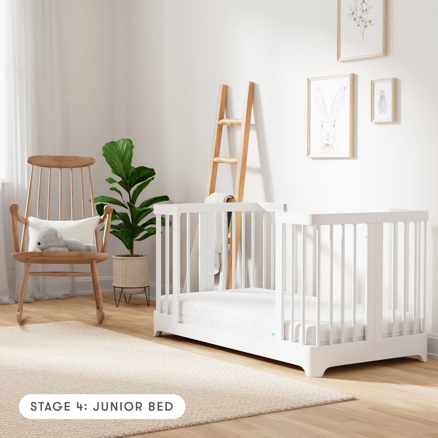 white color Newton Nest Convertible Crib in Junior Bed setting, in nursery next to rocking chair, with text "Stage 4: Junior Bed"