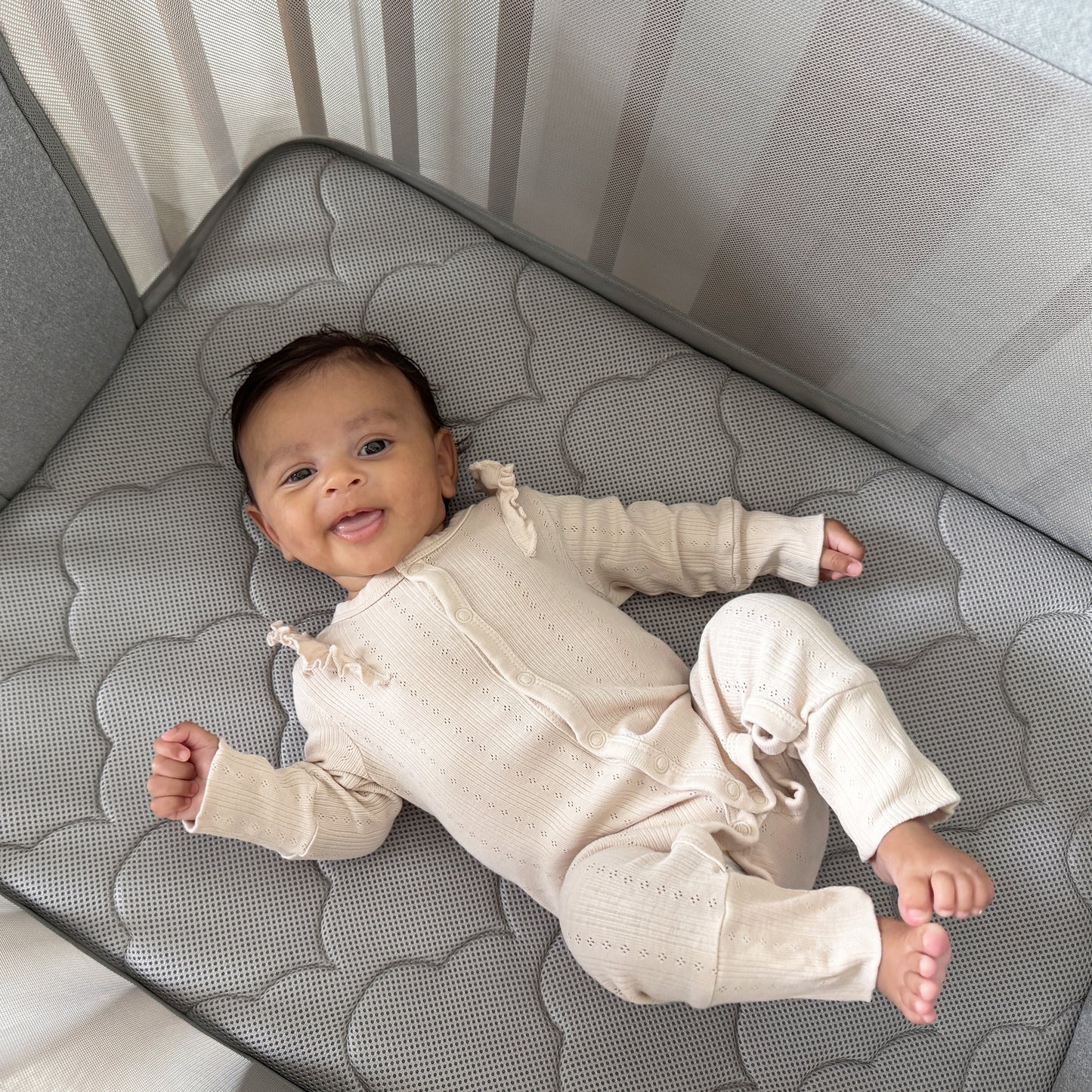 baby lying on Newton Nest Convertible Crib in bassinet setting on bassinet mattress with mesh panels.