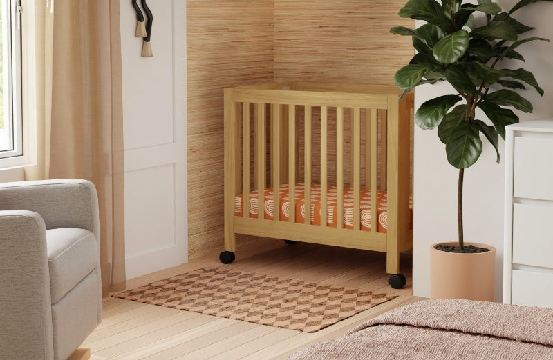 A cozy nursery room featuring a wooden crib with orange patterned bedding, next to a fiddle leaf fig tree and a comfortable gray armchair.