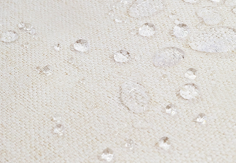 Close-up image of a waterproof beige fabric with scattered clear water droplets demonstrating water resistance.