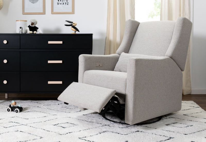 Modern nursery with a stylish light gray glider chair with extended footrest, a black dresser with toys and decor, and a plush white and gray carpet.
