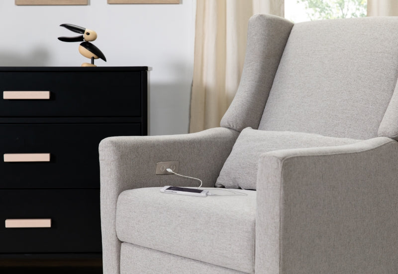 A cozy nursery featuring a modern grey armchair beside a sleek black dresser, decorated with a whimsical bird figure on top.