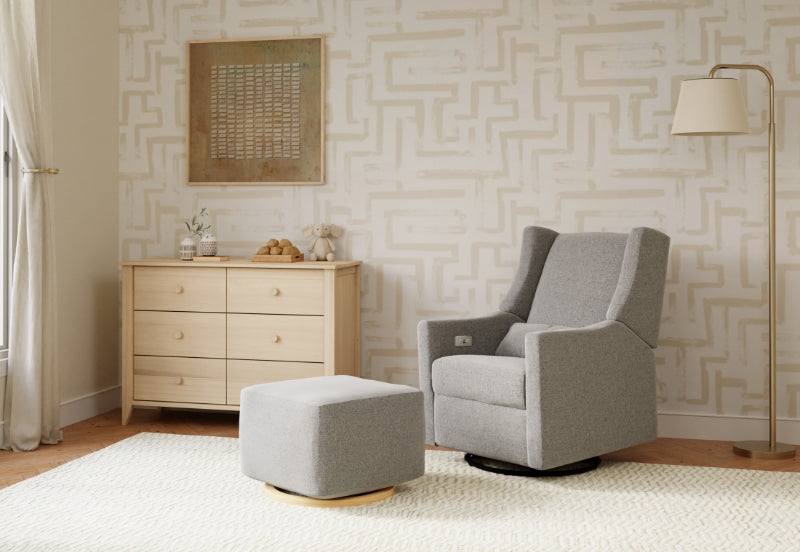 A cozy nursery featuring a modern gray rocking chair with a matching ottoman, a wooden dresser, and neutral decor.