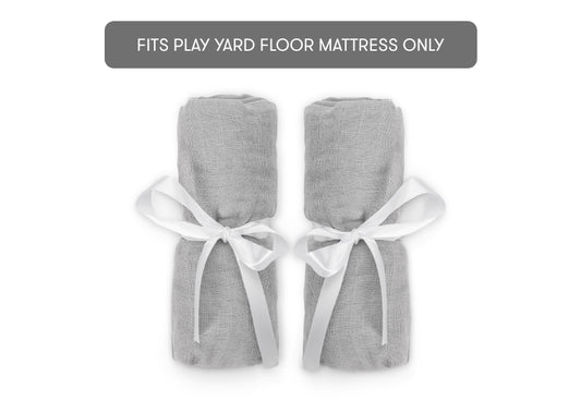 Two rolled-up gray Travel Crib & Play Yard Sheets tied with white ribbons, shown beneath a gray banner reading "FITS PLAY YARD FLOOR MATTRESS ONLY," perfect for play yard or cotton muslin sheets.
