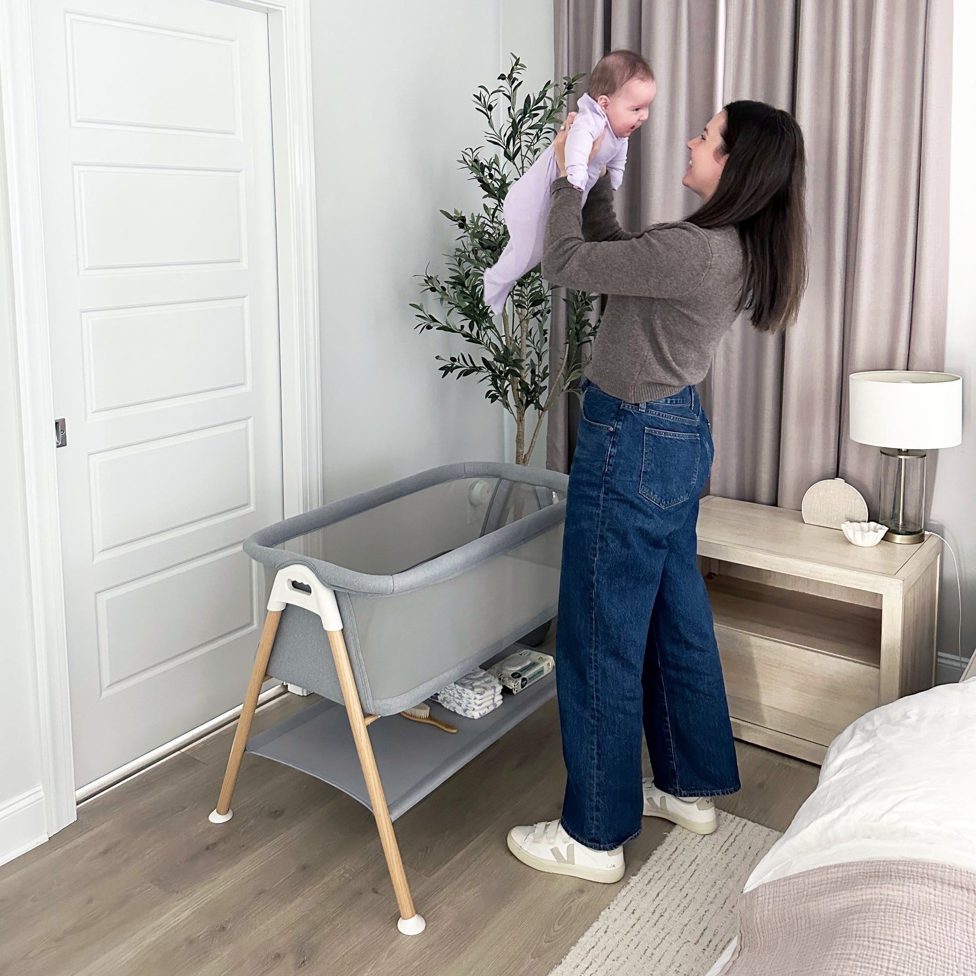 Mom proudly holding up smiling baby above newton essential bassinet.