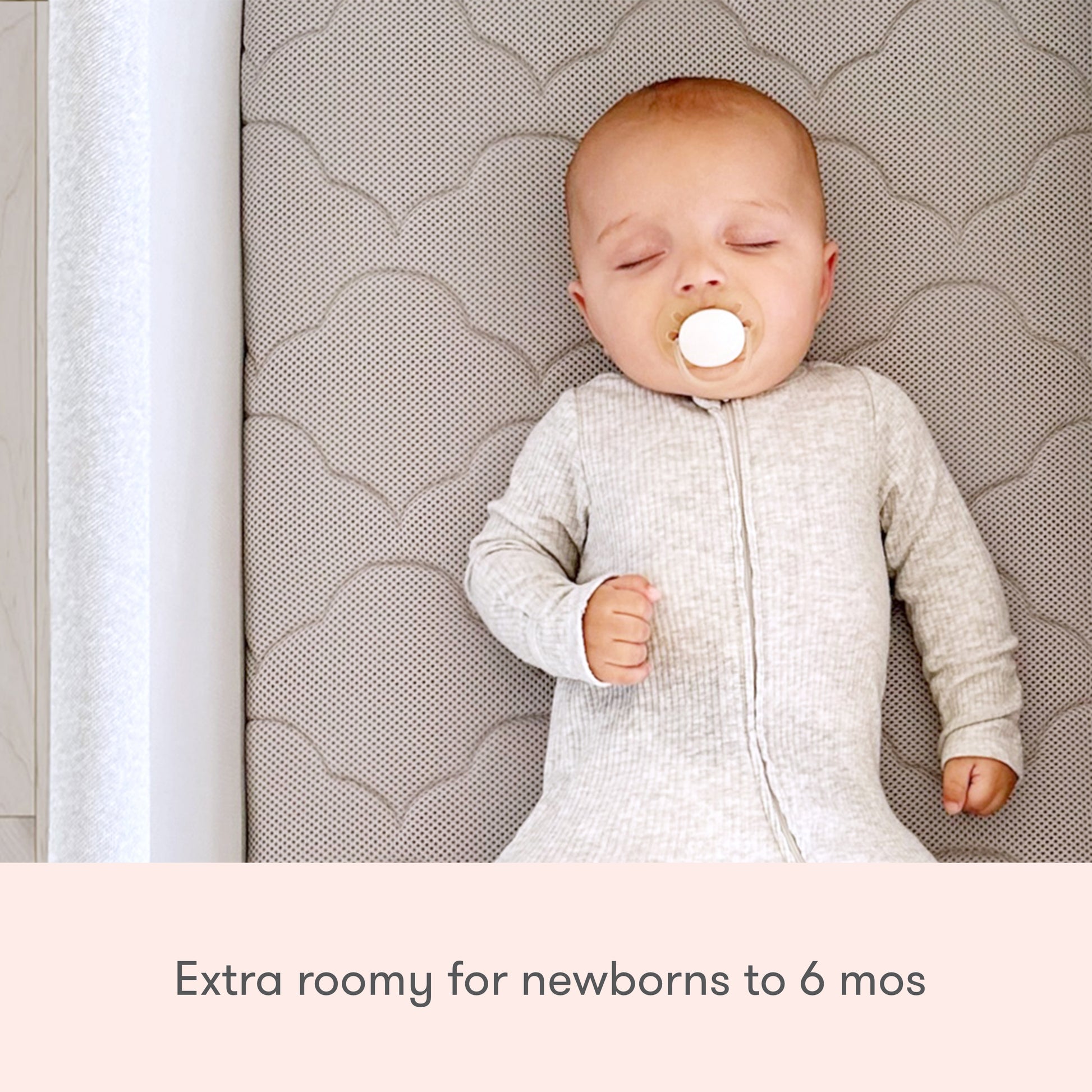 Baby sleeping peacefully in essential bassinet with pacifier in mouth, text reads "extra roomy for newborns to 6 mos"