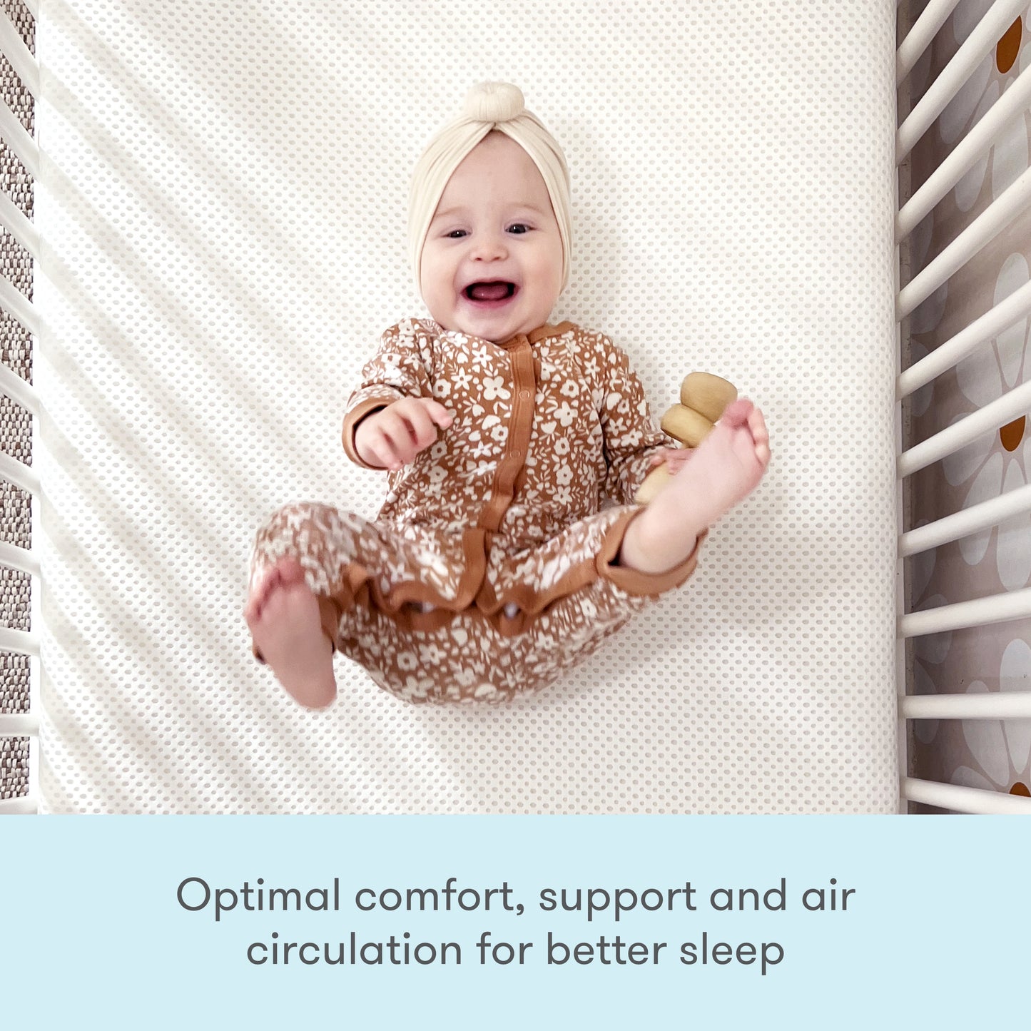 Smiling baby lying on a textured mat wearing a onesie, with text stating 'Optimal comfort, support and air circulation for better sleep'.