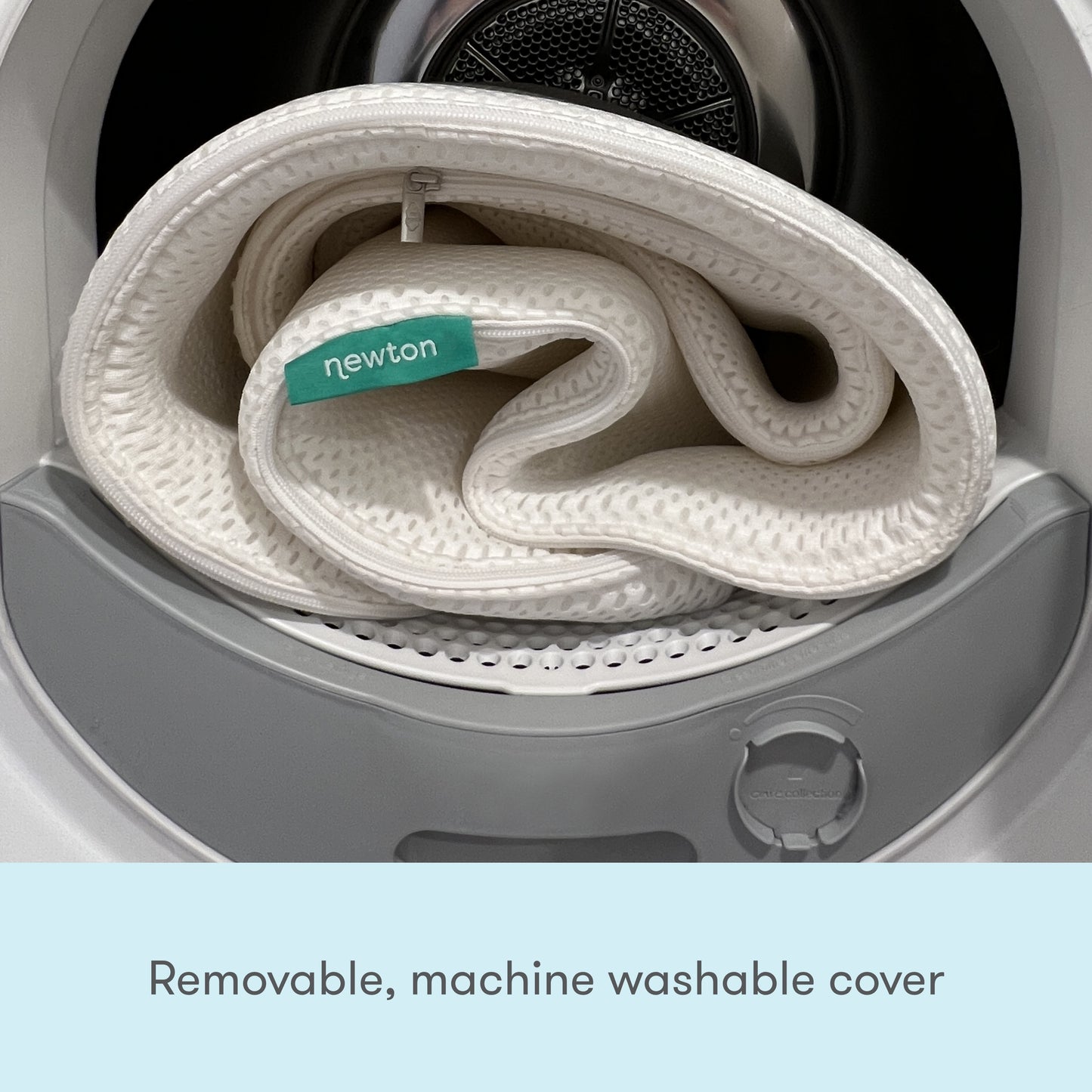 A Newton baby mattress cover with a tag, coiled inside a washing machine, depicting its removable and washable feature, accompanied by the text "Removable, washable cover."
