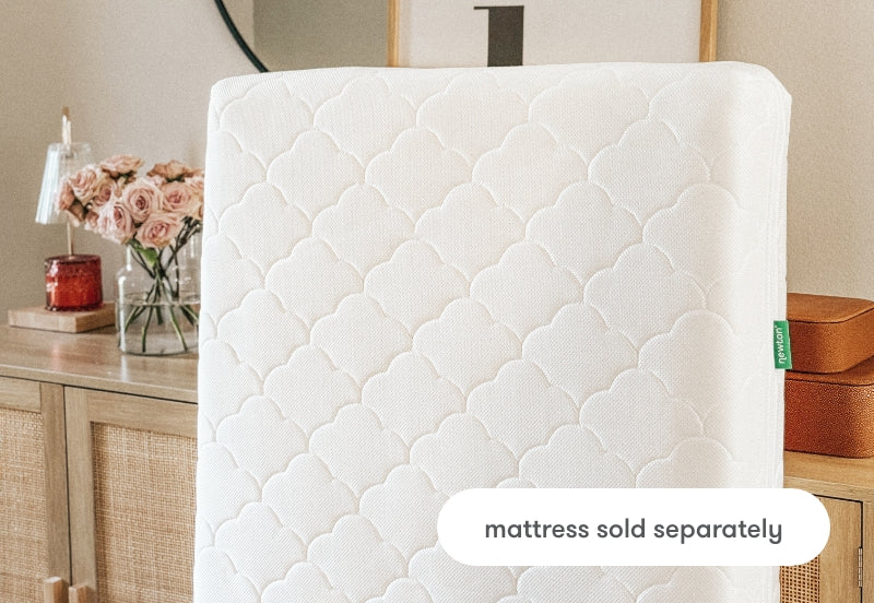 White baby mattress with a patterned cover displayed in a home setting, text overlay reads "mattress sold separately".