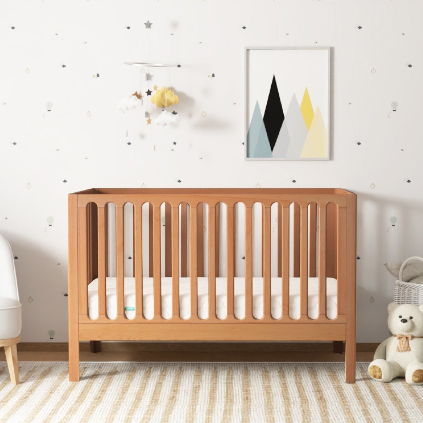 A serene nursery featuring a wooden crib, a cozy white armchair, a plush teddy bear, and decorative accents like a cloud and star mobile and abstract wall art. 999-8420-CST