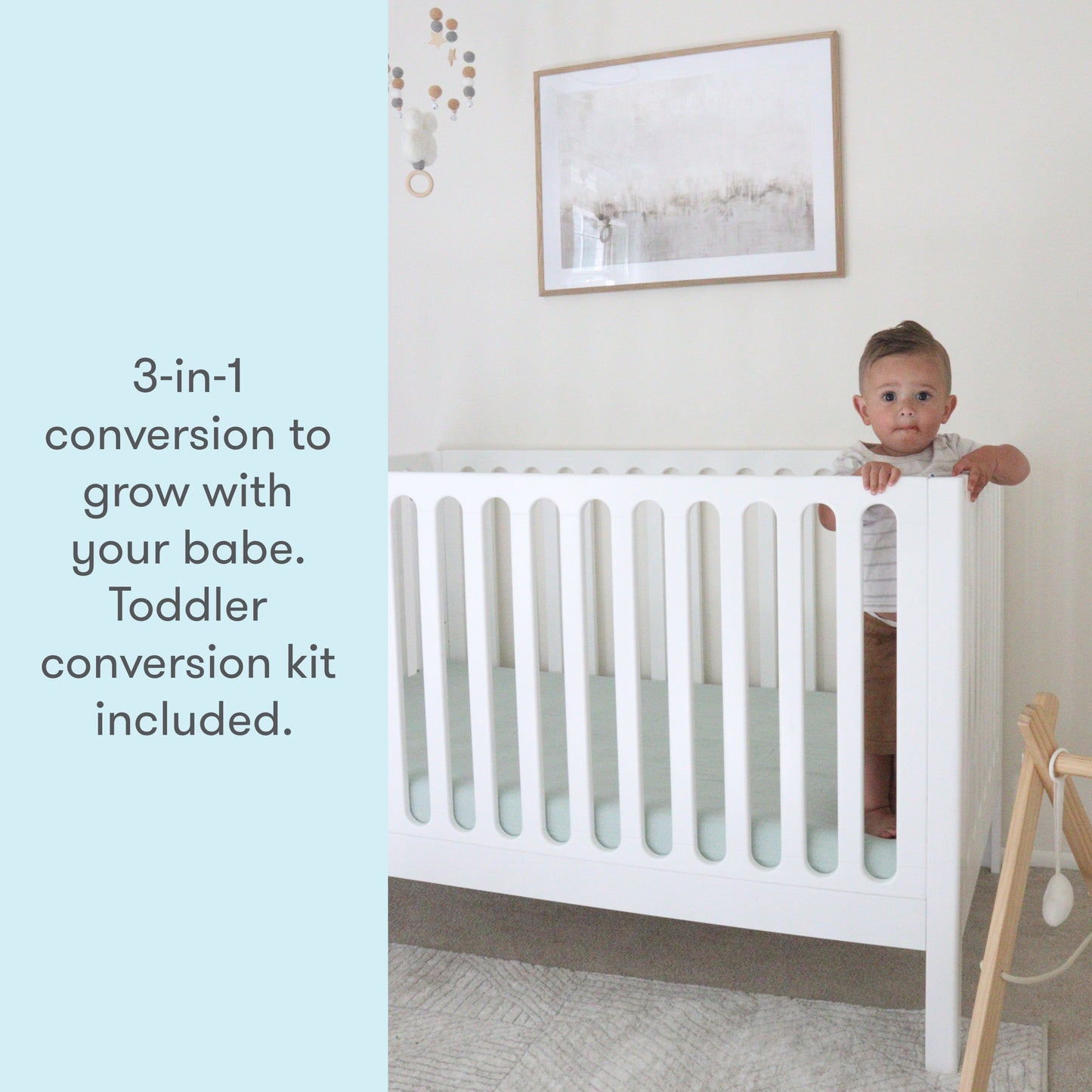Toddler peeking over the side of a white 3-in-1 convertible crib, with text stating "3-in-1 conversion to grow with your babe. Toddler conversion kit included."