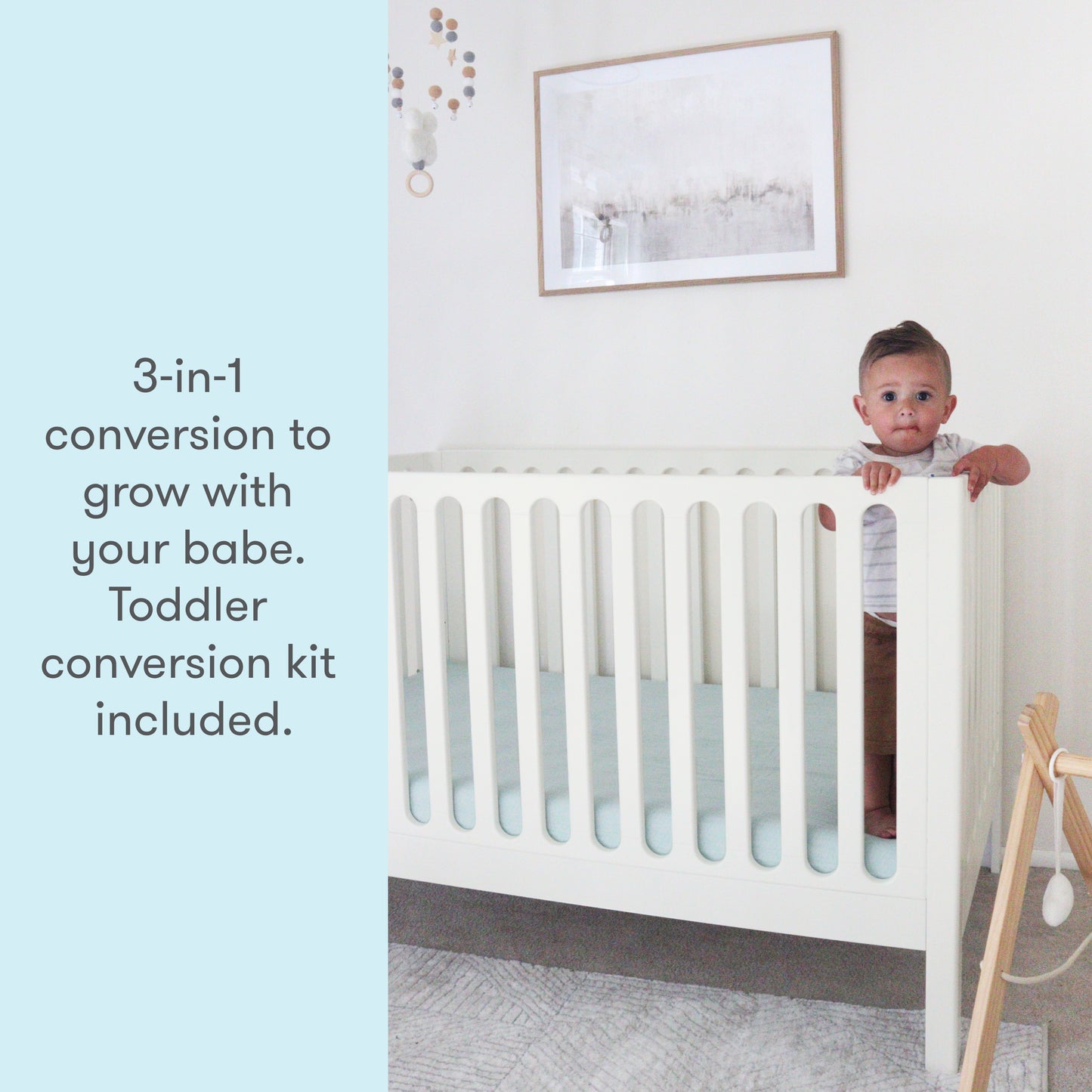 Toddler peeking over the side of a white 3-in-1 convertible crib, with text stating "3-in-1 conversion to grow with your babe. Toddler conversion kit included."