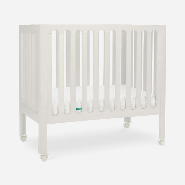 The Newton Baby Galileo Mini Crib with Newton Mattress, featuring vertical slats and four wheels, is crafted from solid Beech wood and shown on a plain white background.