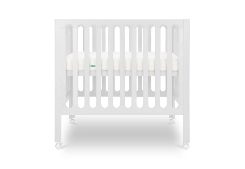White modern crib on wheels with visible mattress, isolated on a plain background.