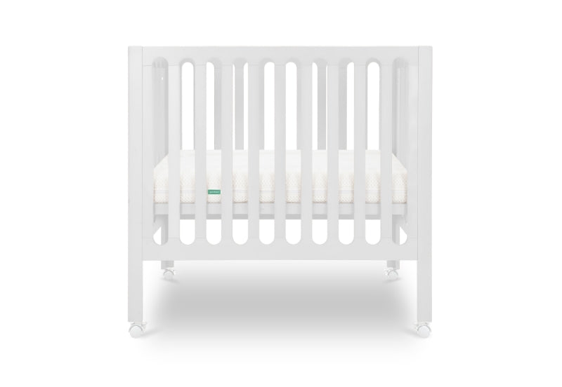 White modern crib on wheels with visible mattress, isolated on a plain background. Mattress in lowered position.