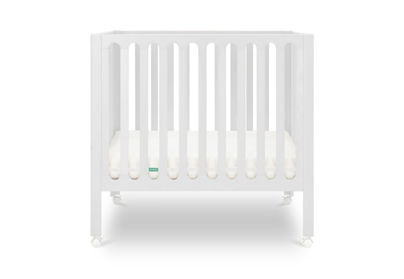 White modern crib on wheels with visible mattress, isolated on a plain background. Mattress in lowest position.