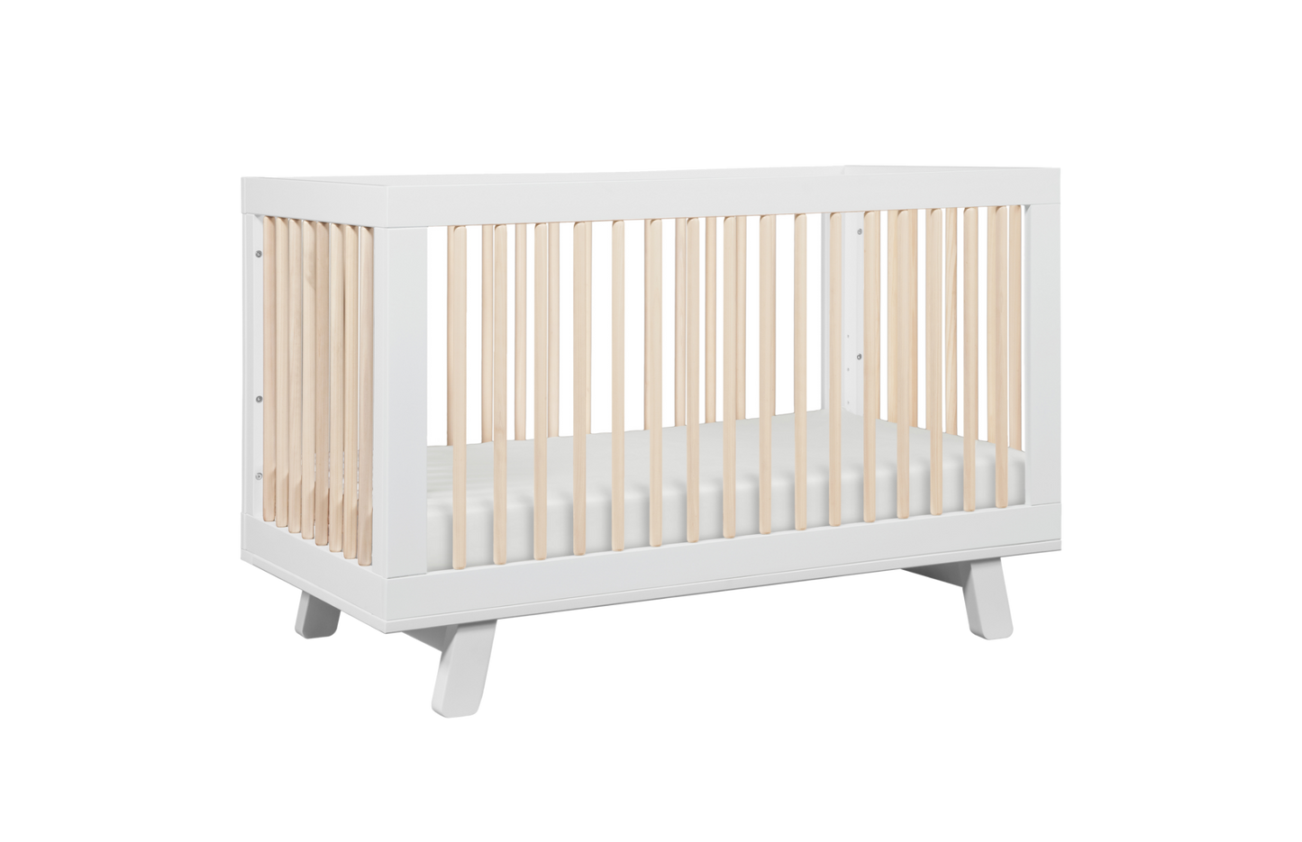 The Babyletto Hudson Convertible Crib features a white frame with light wood slats and includes a white crib mattress, displayed on a plain white background.