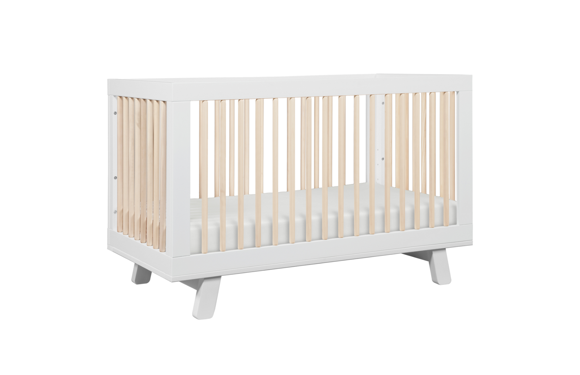 The Babyletto Hudson Convertible Crib features a white frame with light wood slats and includes a white crib mattress, displayed on a plain white background.