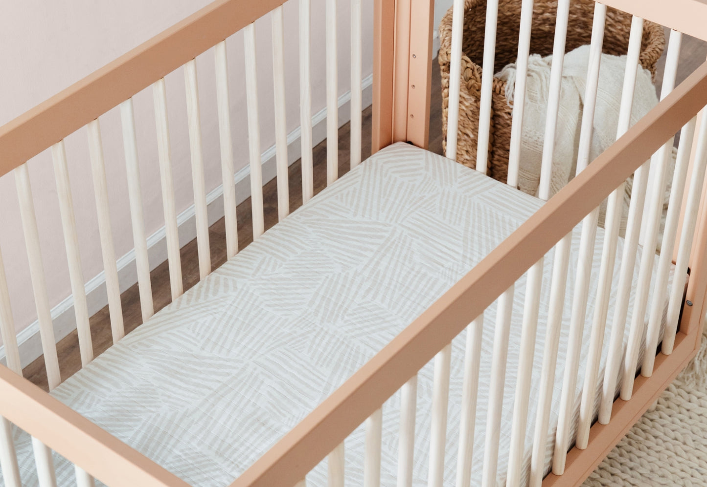 Wooden baby crib with light cream and gray patterned mattress in a softly lit room, providing a comfortable and stylish sleeping environment for infants.