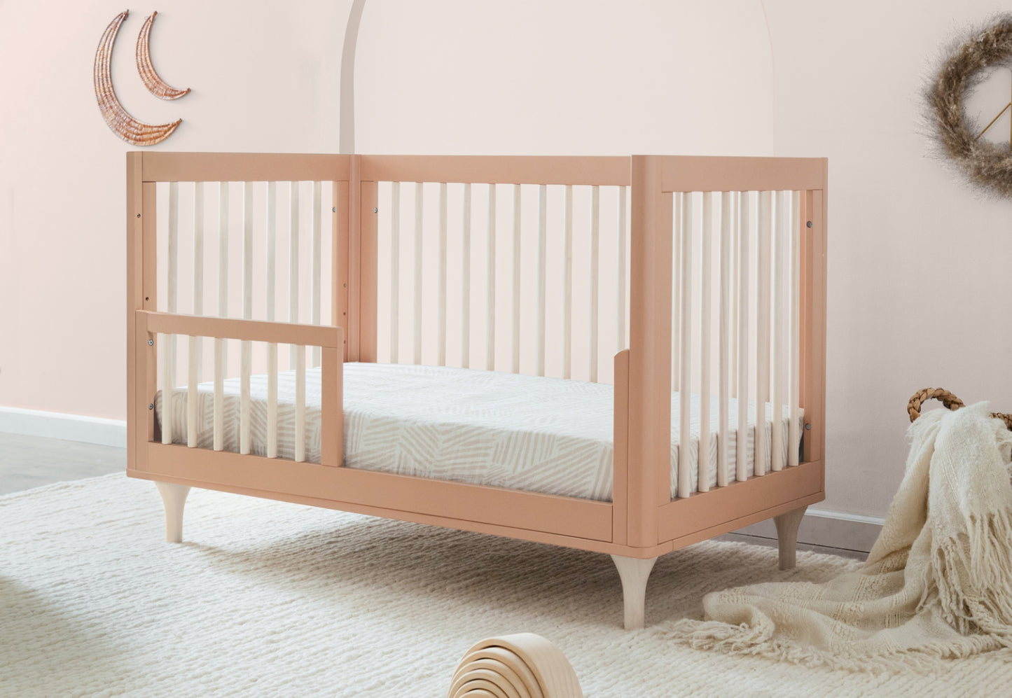 Stylish peach-colored crib in a serene nursery setting with decorative moon wall art and cozy accents.