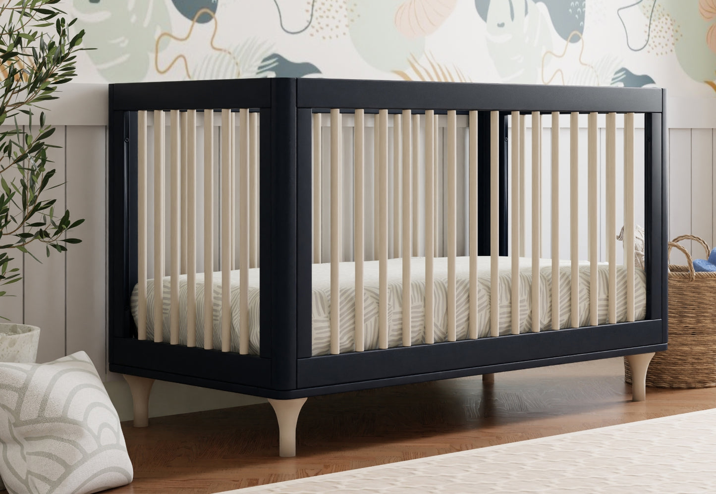 Modern navy blue crib in a nursery room decorated with a whimsical wall mural and natural accents.