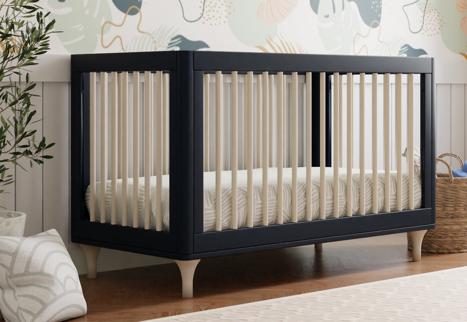 Modern navy blue crib in a nursery room decorated with a whimsical wall mural and natural accents.