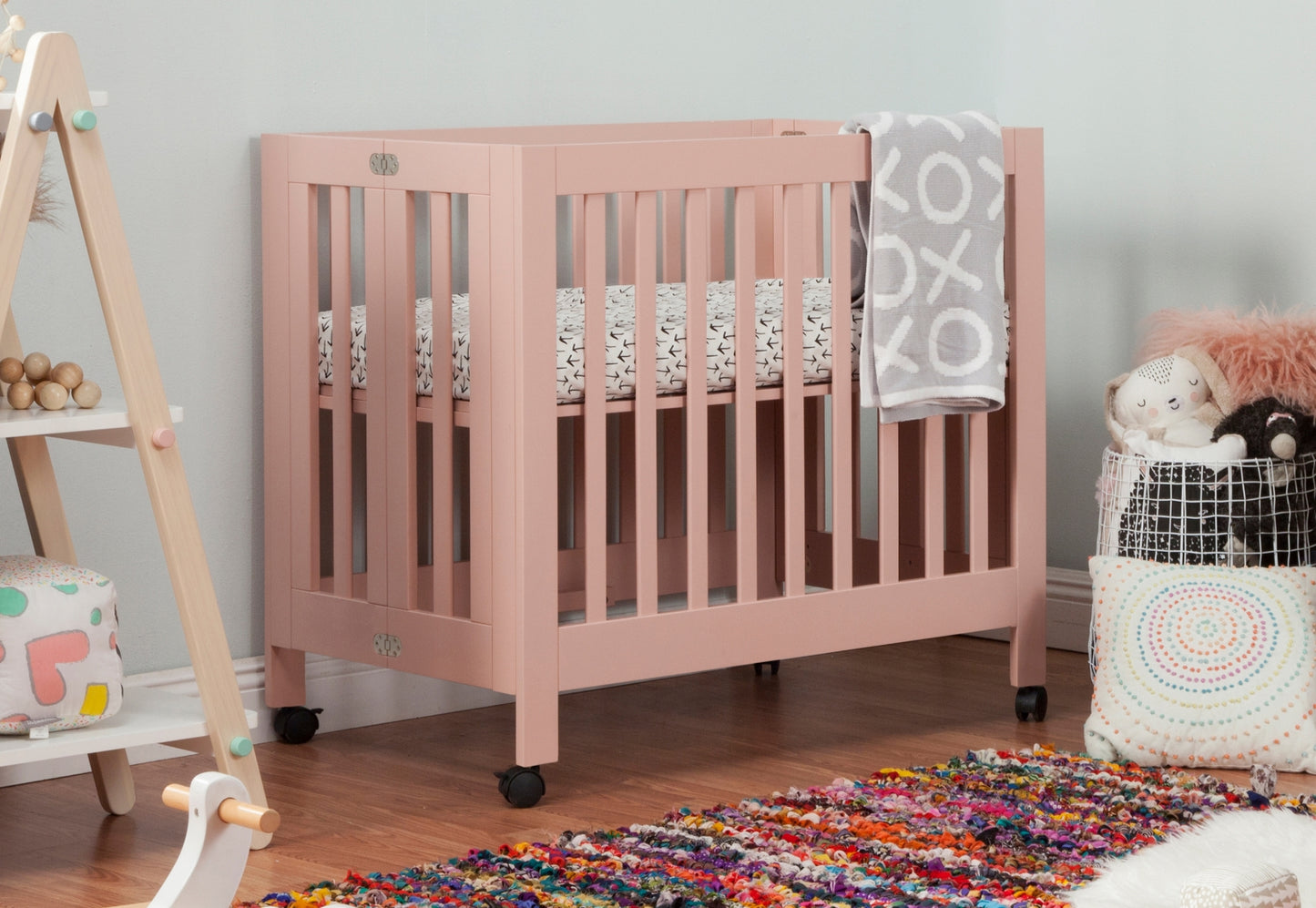 A cozy nursery room featuring a pink crib with stylish blankets and a playful assortment of children's toys and pillows, creating a warm and inviting atmosphere.