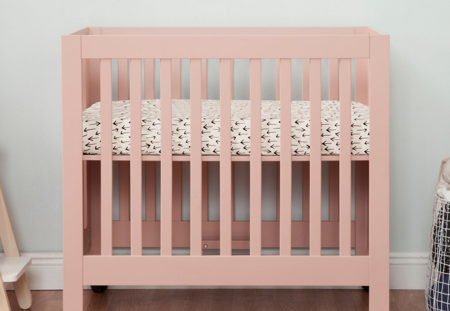 A soft pink baby crib with a patterned mattress in a cozy room setting.