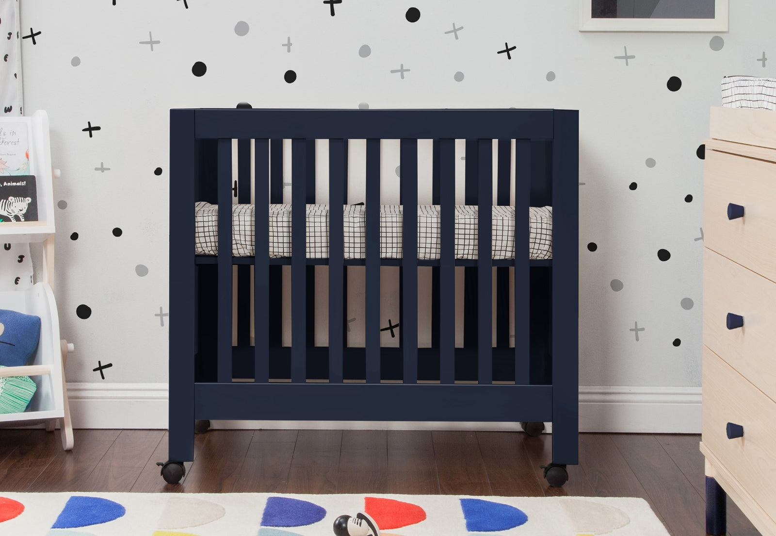 Navy blue baby crib in a nursery with playful black and white wall decals and a colorful circular patterned rug.