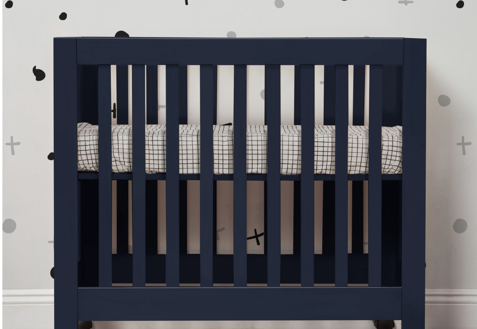 A navy blue crib with a grid-patterned bedding set against a wall adorned with black and plus sign decals.