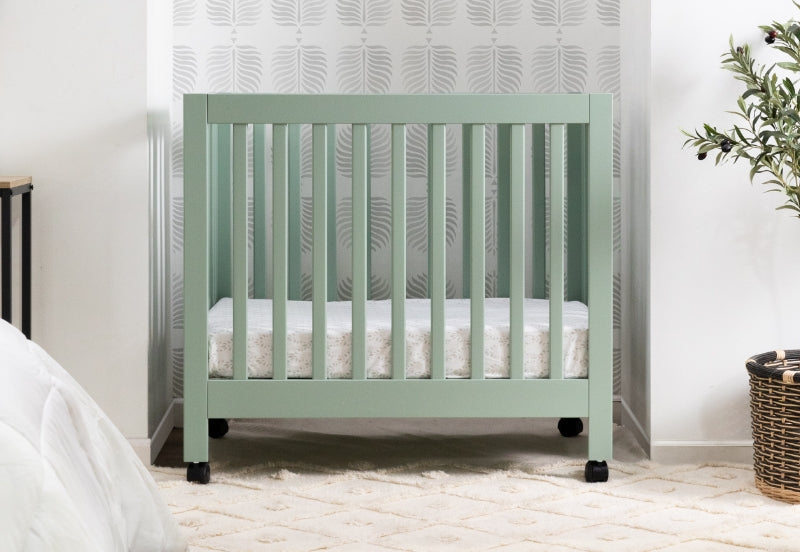 A minimalist style nursery featuring a mint green crib against a patterned wallpaper, complemented by a natural toned rug and a plant. 999-8505-LSG