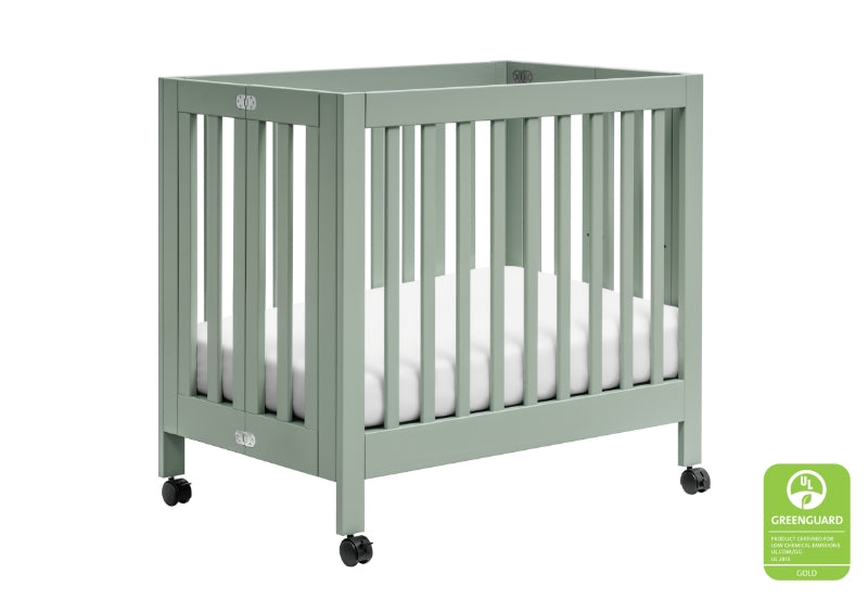 Green toddler crib on wheels, featuring a minimalist design and a "GREENGUARD Gold certified" label on the lower right.