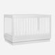 A modern white baby crib with vertical slats and a solid base.