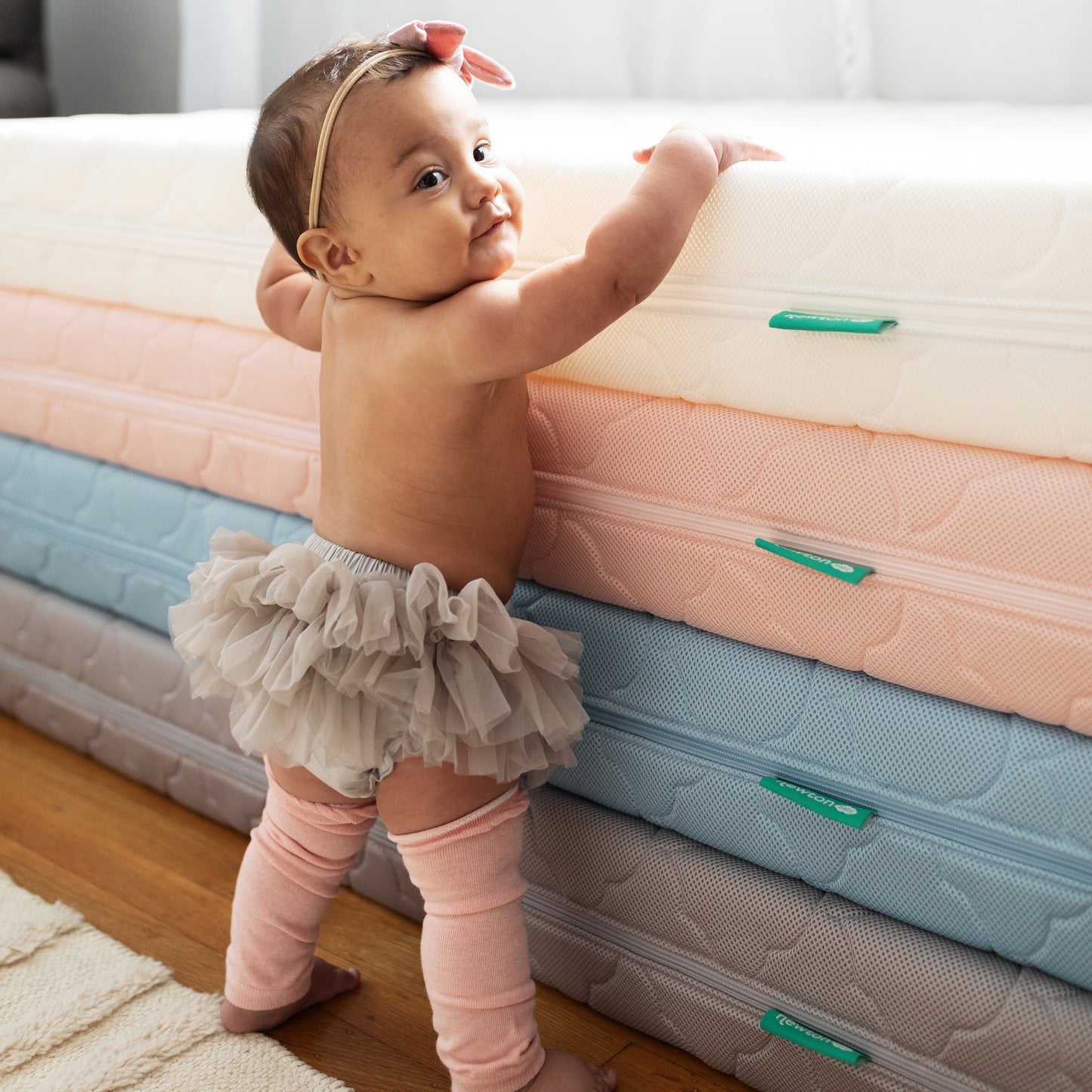 baby standing next to stack of multi-colored newton mattresses