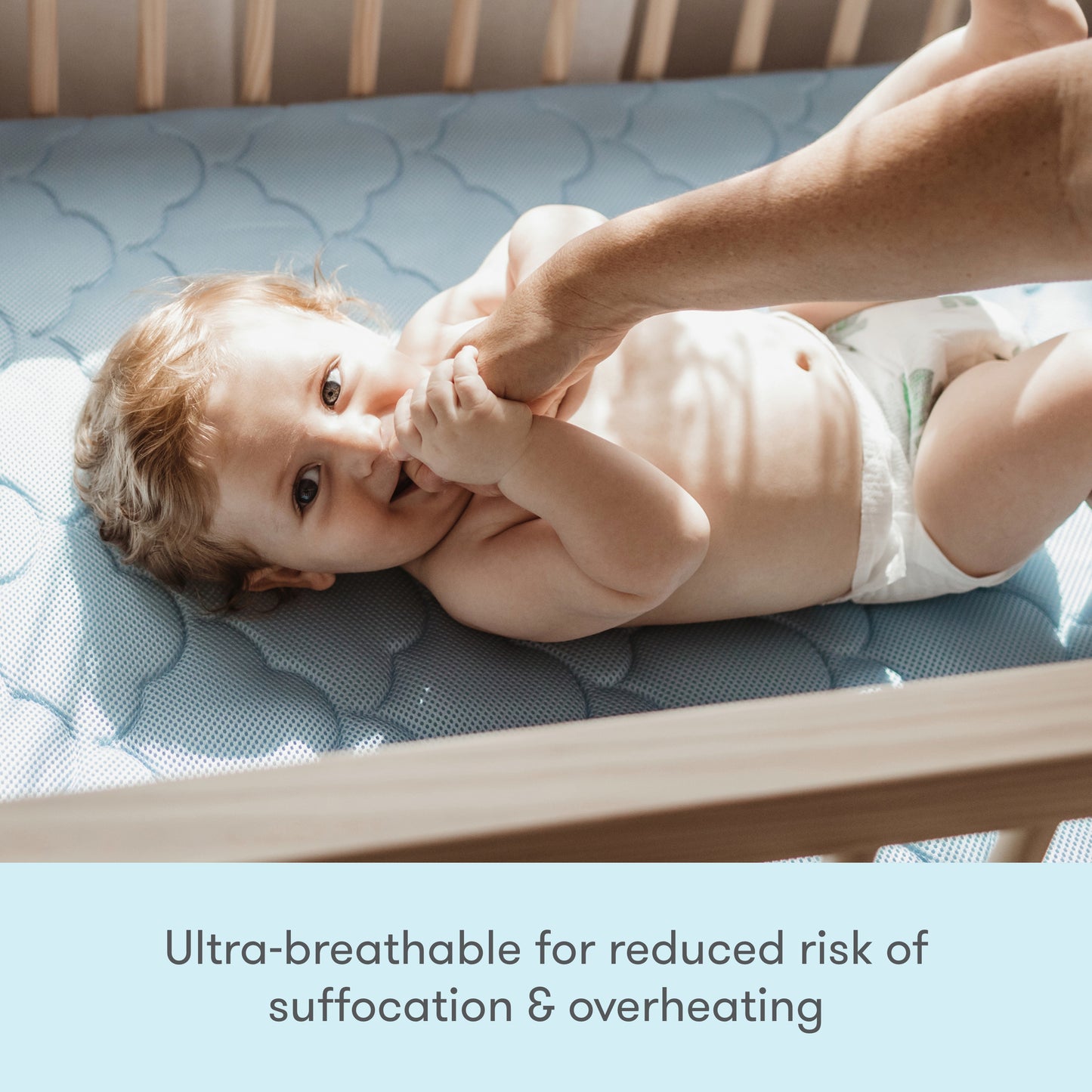 Image of a baby wearing a cute outfit, lying on a mattress, with text stating "Ultra breathable for reduced risk of suffocation & overheating."